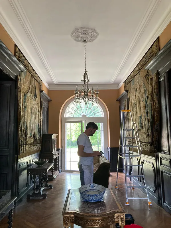 André Slijkhuis aan het werk in een monumentale hal met wandtapijten en een kroonluchter